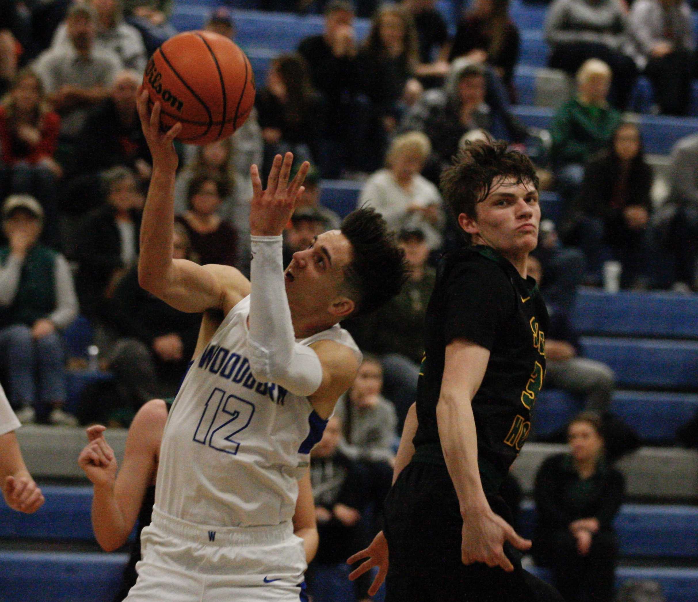 Woodburn's R.J. Veliz corkscrews past Sweet Home's Jake Swanson for two of his game high 23 points. (Photo by Norm Maves Jr.)